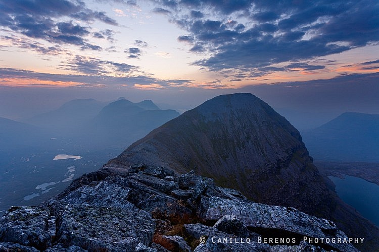 Spectacularly shaped mountains form a stunning backdrop behind Sail Mhor and Lochan Coire Mhic Fhearchair on the right of it. The haze, which was present all day, added to the atmosphere during the post-sunset blue hour, creating soft light rendering the distant mountains in a subtly layered way.