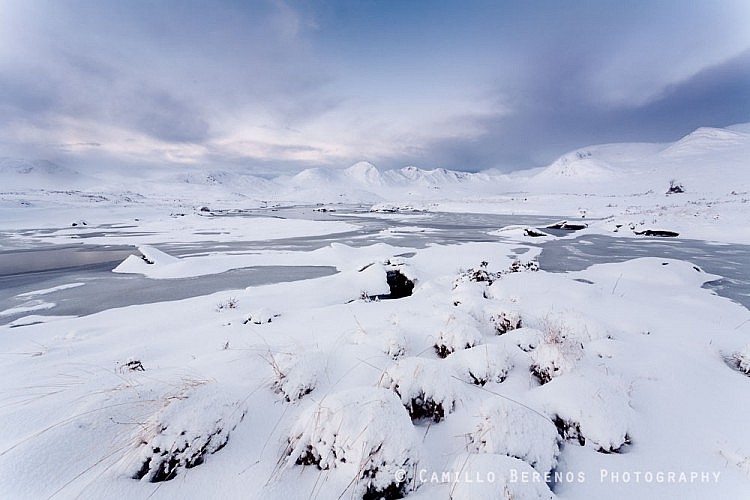 A partially frozen Lochan na Stainge with the snow-covered mountains of Black Mount behind