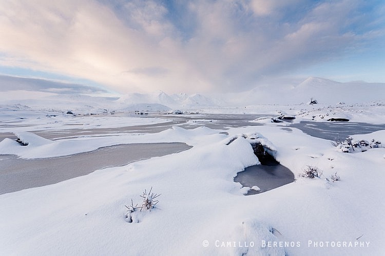 Soft morning light over a frozen Lochan na Stainge and snow-covered Black Mount mountains