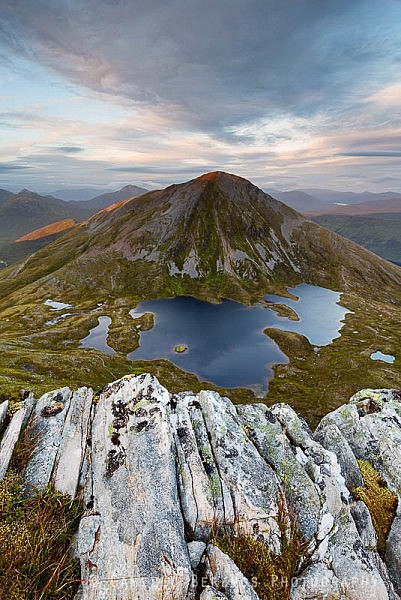 Sgurr Eilde Mor partially turning red by the setting sun with rocks on Sgor Eilde Beag in the foreground