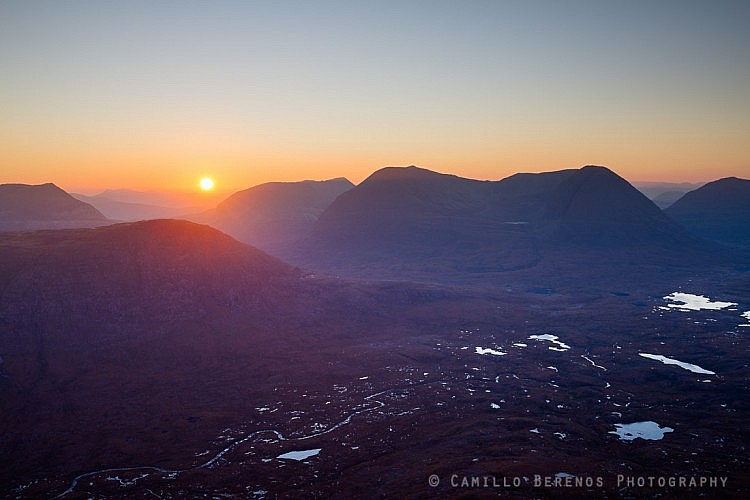 The sun rising above the rugged landscape of Torridon with Beinn a 'Chearcaill and Beinn Eighe towering high above the moorland.