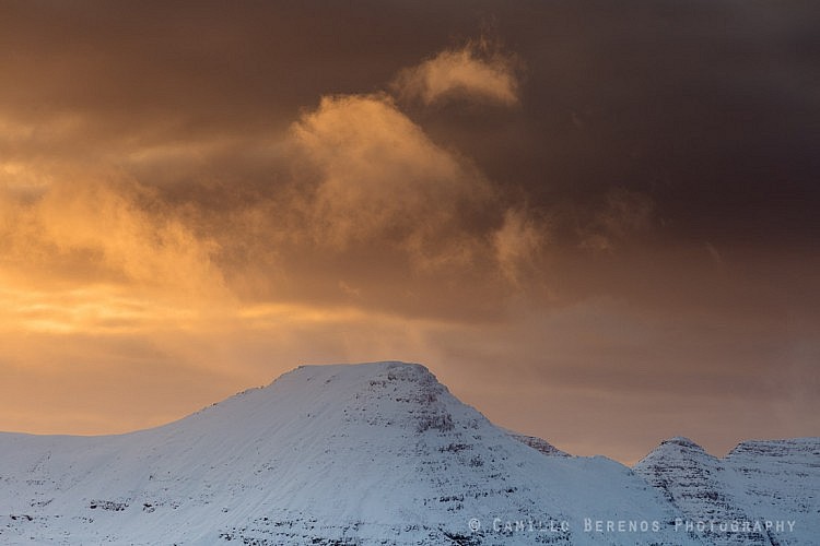 Brightly lit clouds above Beinn Dearg stand out against a backdrop of dark snow clouds at sunset in winter