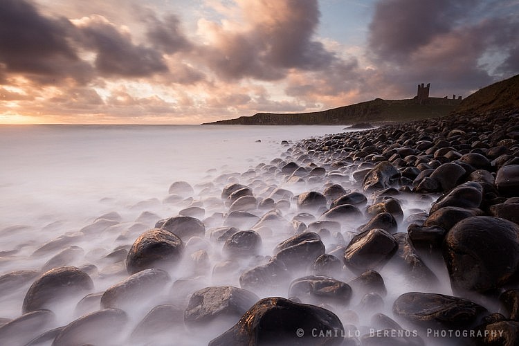 Stormy seas at Embleton Bay with Dunstanburgh Castle perched high on the cliffs beyond