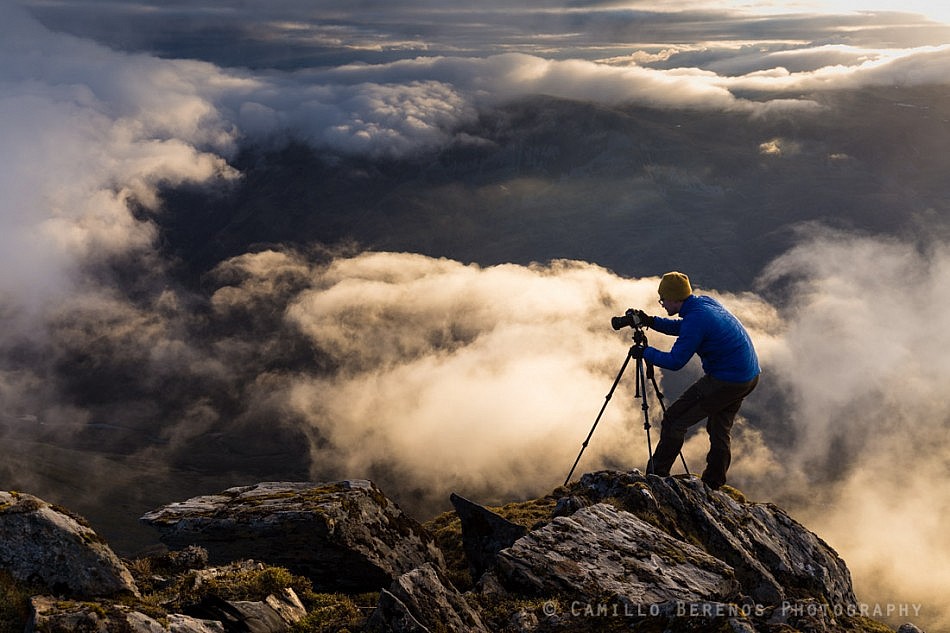 A landscape photographer setting up for his shot above the clouds on a steep cliff in the Scottish Highlands (Sgurr Fhuaran, Five Sisters of Kintail)